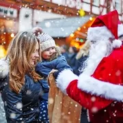 Kleines Kleinkindmädchen mit Mutter auf Weihnachtsmarkt.